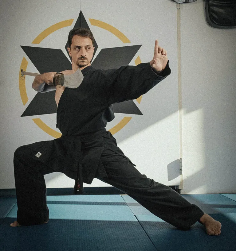 Kung-Fu-Trainer im schwarzen Anzug mit Säbel in tiefer Kampfstellung vor dem Syndicate-Logo